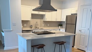 Una cocina moderna con armarios blancos, un refrigerador de acero inoxidable, una isla central con taburetes y una campana extractora grande.