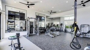 Un gimnasio moderno con varios equipos de ejercicio, espejos grandes y ventiladores de techo.