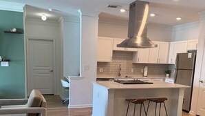 Una cocina moderna con armarios blancos, una campana extractora de acero inoxidable y una isla central con taburetes.