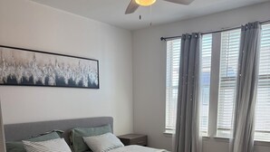 A bedroom with a bed, a nightstand, a ceiling fan, and a window with curtains. - Universal Kids Resort Frisco Cozy 2-bedroom apartment with pool and gym access (Frisco)