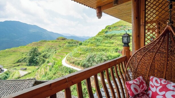 Un balcone in legno con vista su campi a terrazze e montagne.