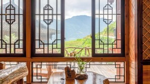 Una camera in legno tradizionale con ampie finestre caratterizzate da elaborate decorazioni a griglia, un tavolo in legno con un vaso di piante verdi e un'atmosfera rustica.
