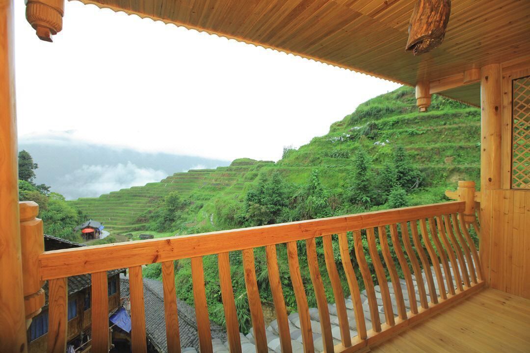 A wooden balcony with a view of terraced fields and a distant village.