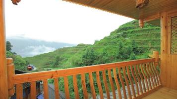 A wooden balcony with a view of terraced fields and a distant village.