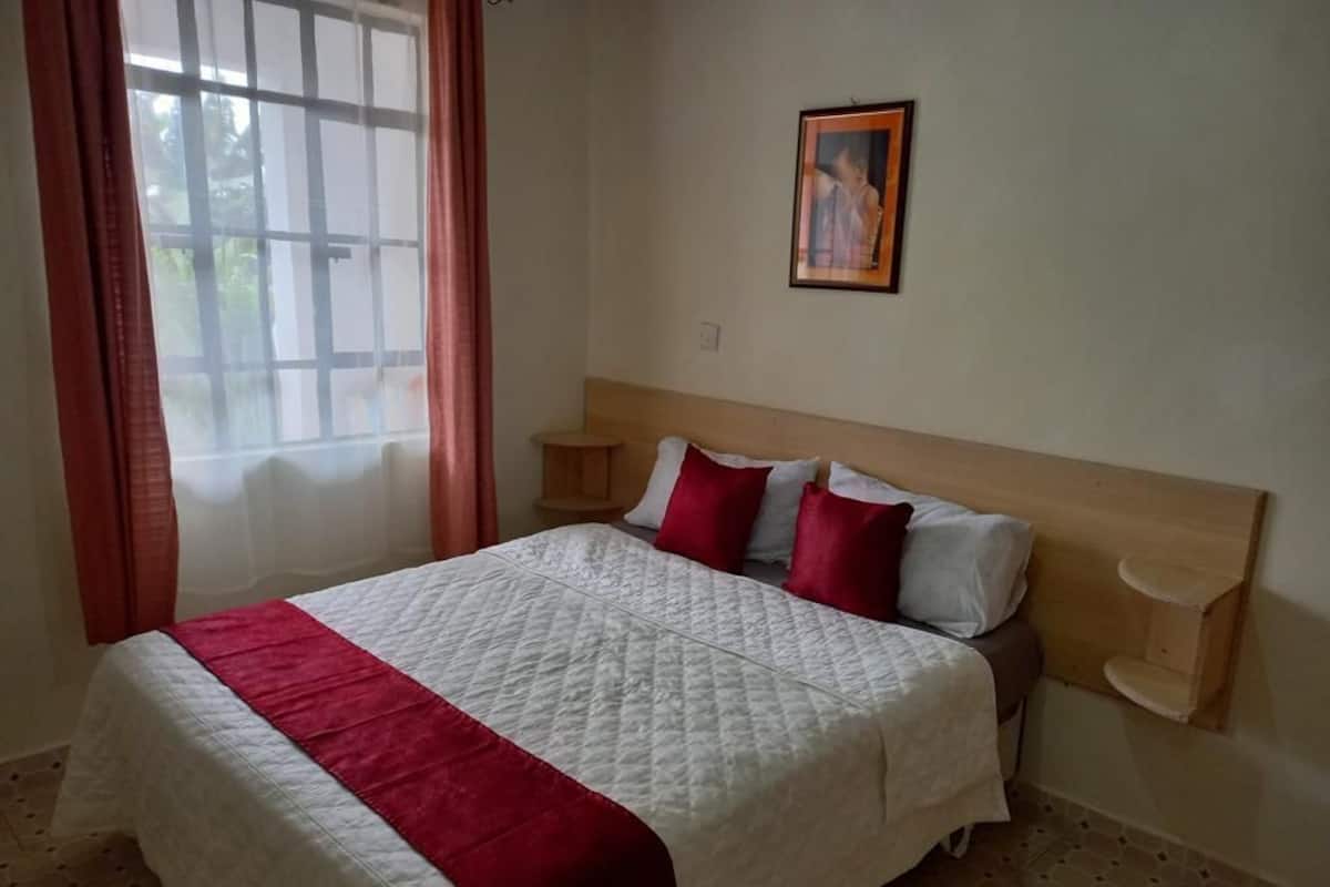 Un lit bien fait, recouvert d’une couvre-lit blanche et rouge, avec deux tables de chevet et un tableau encadré accroché au mur.