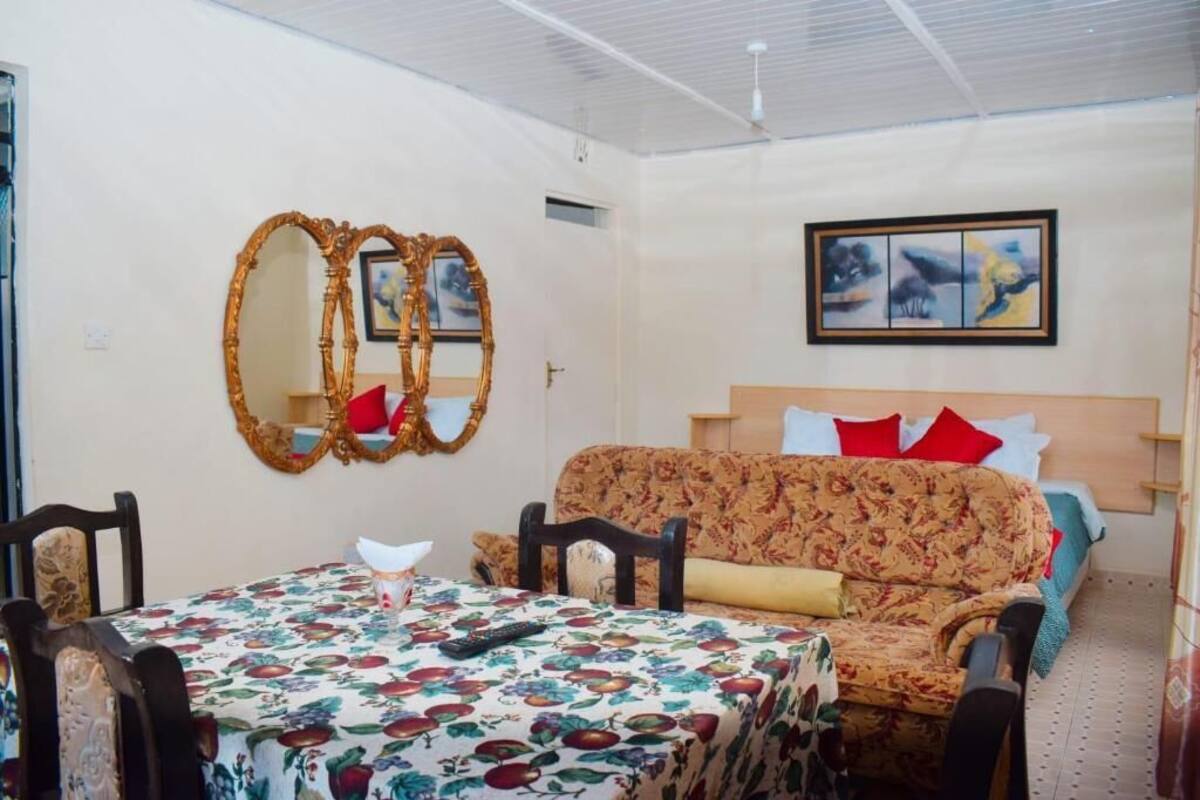 Une pièce avec une nappe à motifs floraux, un canapé avec des coussins rouges, une tête de lit en bois et un tableau encadré au mur.