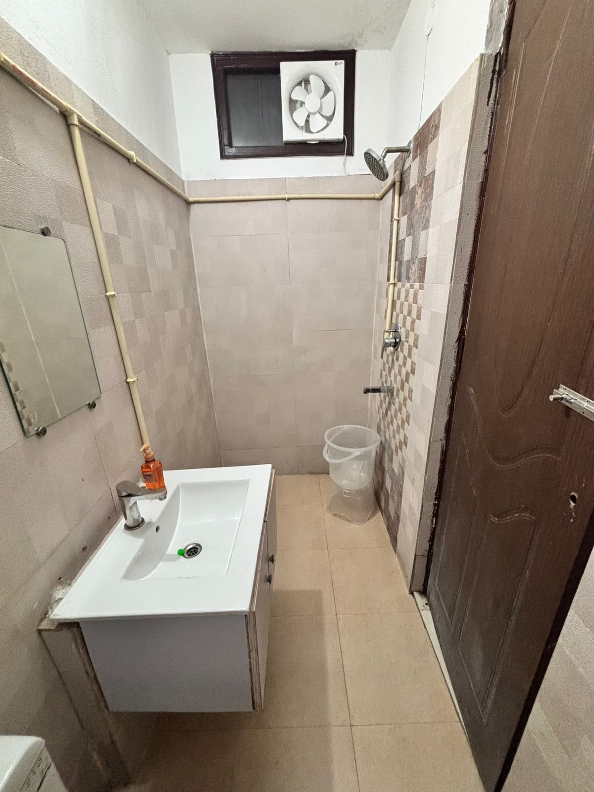 A small bathroom with a white sink, a mirror, a fan, and a shower area.