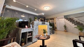 A modern reception area with a marble reception desk, a flat-screen TV, and a staircase leading to an upper floor. - The Shivaay AIIMS by Lovely Hospitality (Rishikesh)