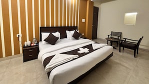 A hotel room with a bed, bedside tables, a desk with chairs, a ceiling fan, and a wall-mounted light. - The Shivaay AIIMS by Lovely Hospitality (Rishikesh)