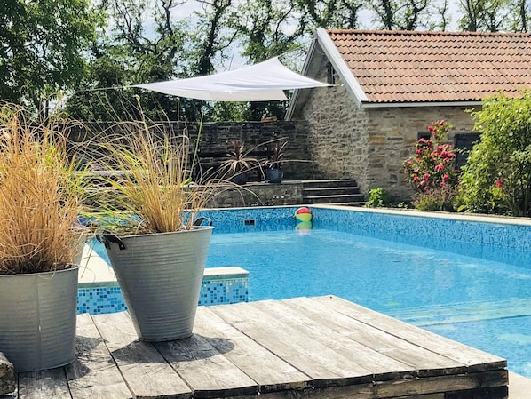 A swimming pool with a wooden deck, surrounded by potted plants and a stone wall. - 4 Person Holiday Home in Morbylanga (Morbylanga)