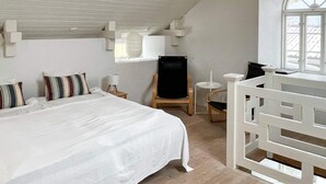 Una camera da letto con un letto grande, una sedia di legno, un tavolino e una ringhiera bianca.