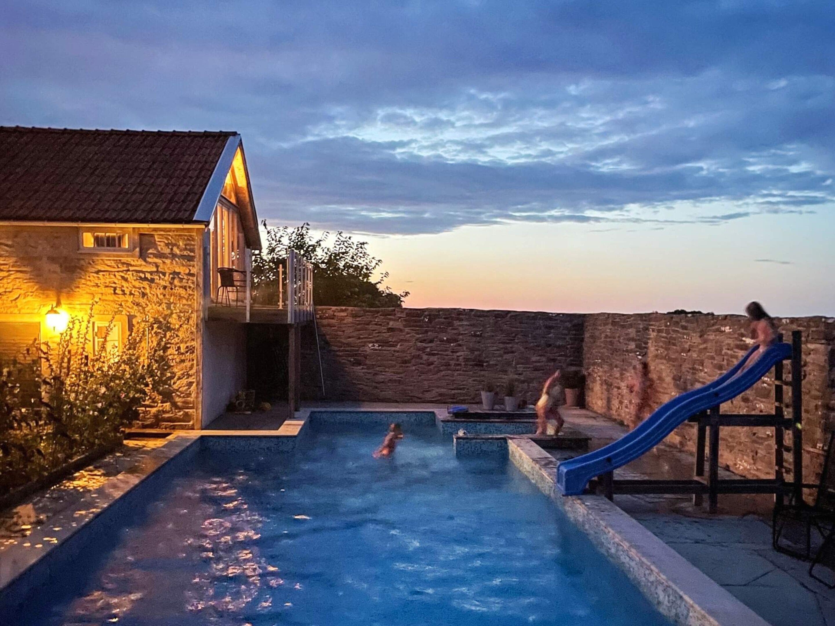 En swimmingpool med vandrutsjebaner, en stenvæg og en bygning med lys.