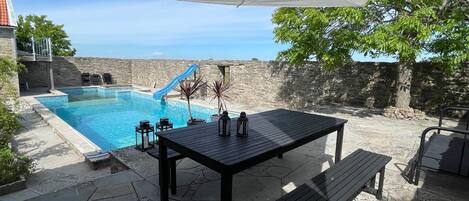 Ein Poolbereich mit Tisch und Bänken, umgeben von Steinmauern und blauem Himmel.