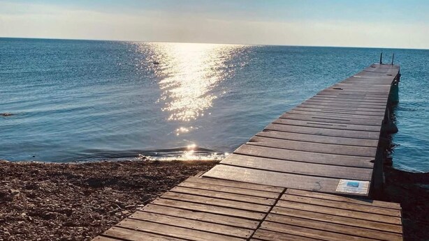 Una banchina in legno che si protende su acque calme sotto un cielo sereno.