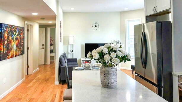 A modern kitchen with a central island, stainless steel appliances, and a dining area with a grey sofa. - 51.Peaceful, modern 3BR Home Near Encore Casino, 12min to Boston (Everett)
