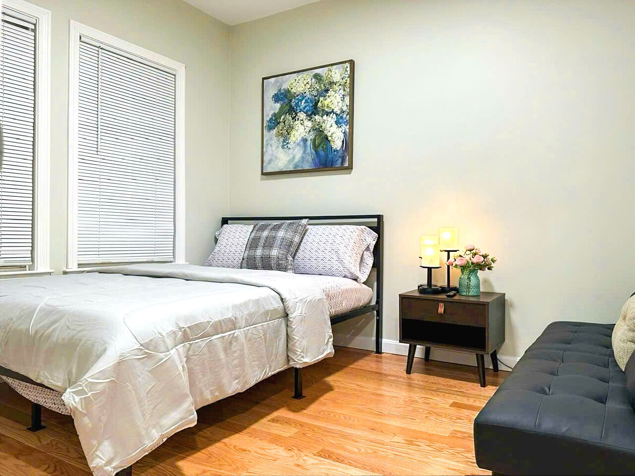 A bedroom with a bed, bedside table with lamps, a nightstand, and a sofa.