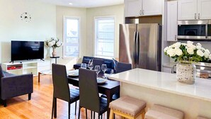 A modern kitchen with stainless steel appliances, a dining area with a table set for two, and a living area with a sofa and TV. - 51.Peaceful, modern 3BR Home Near Encore Casino, 12min to Boston (Everett)