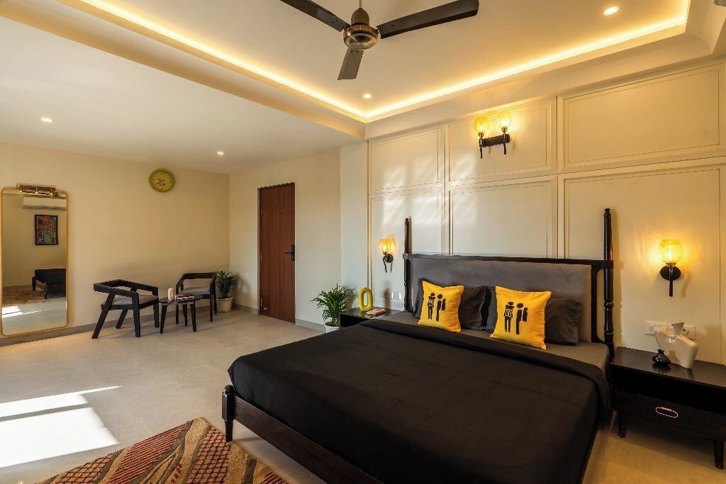 A modern bedroom with a large bed, bedside lamps, a ceiling fan, and a seating area with chairs and a small table.