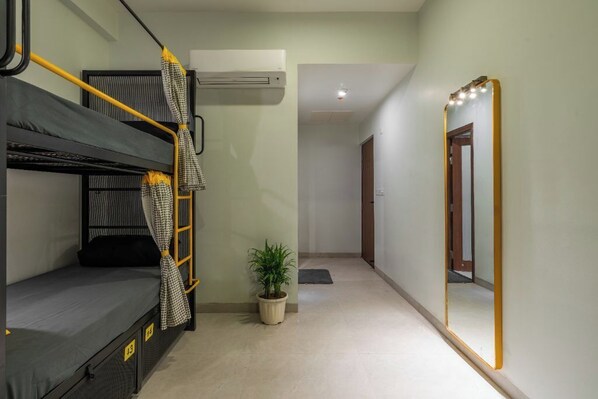 A dormitory room with bunk beds, a potted plant, a mirror, and an air conditioning unit.
