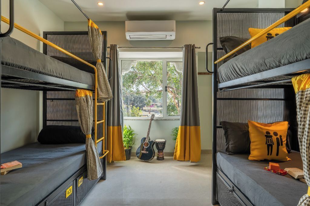 A dormitory room with bunk beds, a window with curtains, a guitar, and a drum.