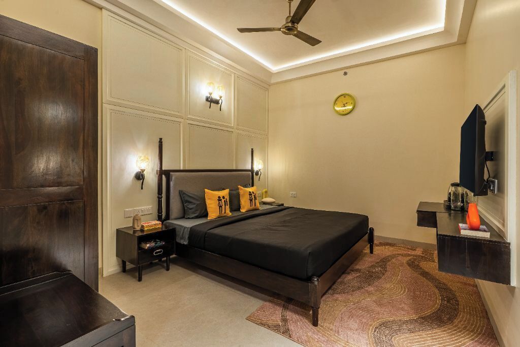 A bedroom with a bed, nightstands, a ceiling fan, a clock, and a TV.