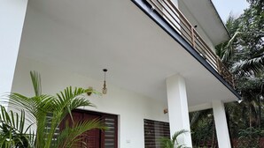 A modern house with a covered porch, potted plants, and a wooden staircase. - Grovestay (Kannur)