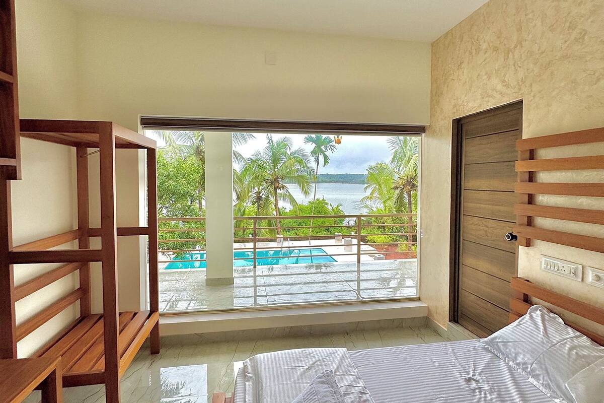 Un dormitorio con cama, ventilador de techo, vista a una piscina y palmeras, y cabecera de madera.