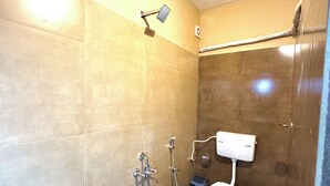 A small, compact bathroom with a shower, toilet, and a bucket. - Grovestay (Kannur)