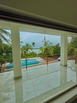 Vista desde un balcón con piscina, palmeras y una masa de agua.