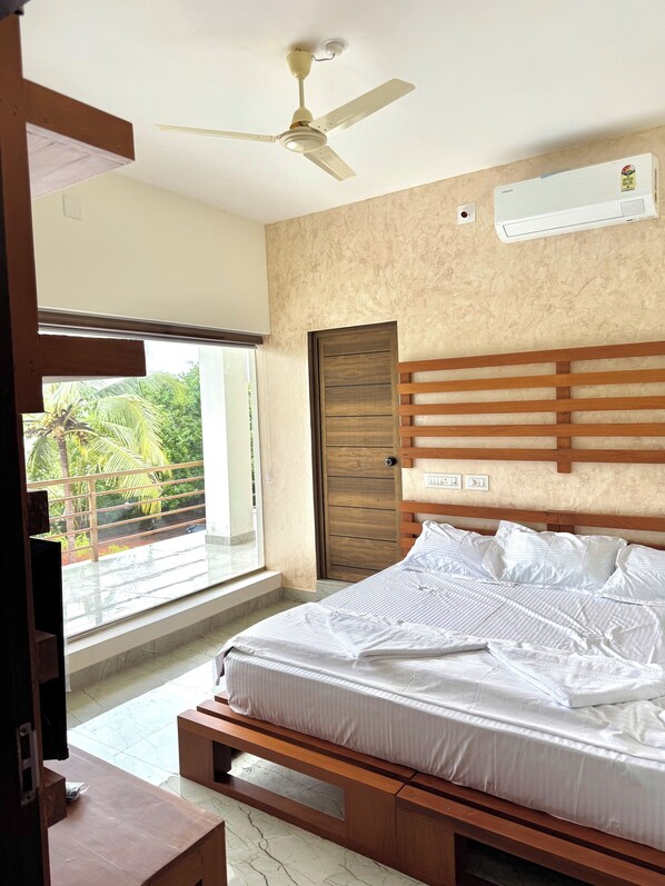 Un dormitorio con cama, cabecera de madera, ventilador de techo, aire acondicionado y vistas al exterior.