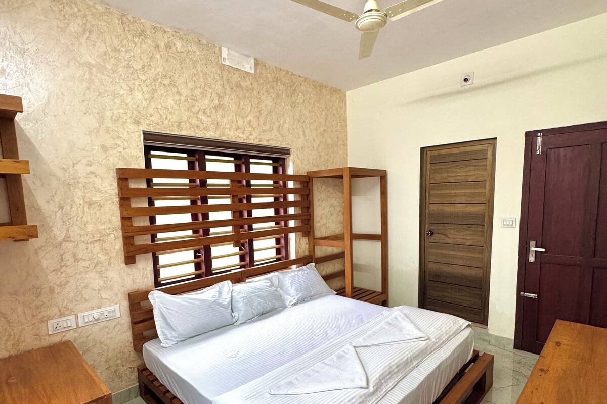 Un dormitorio con cama de madera, ventilador de techo, armario de madera y una mesita de madera.