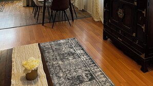 Un comedor con una mesa, sillas, un ventilador de techo, un mueble de madera oscura y una alfombra estampada.