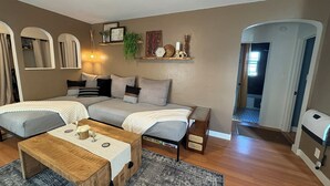 Una sala acogedora con un sofá, una mesita de centro y una alfombra. Hay una puerta que conduce a otra habitación.