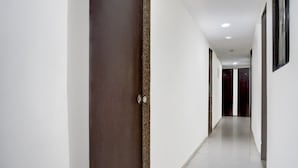 Un lungo e stretto corridoio con pareti bianche e una porta in legno scuro sulla sinistra.