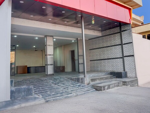 L’entrée d’un immeuble se distingue par un auvent rouge, un mur en briques et un escalier menant à une porte.