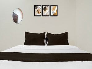 A bedroom with a bed, two black pillows, a white and black bedspread, and three framed wall art pieces above the bed.