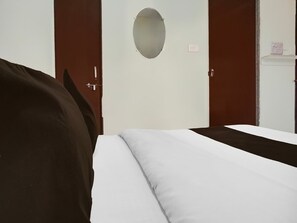 Une chambre d’hôtel avec un lit, une armoire et une petite table équipée d’une prise électrique.