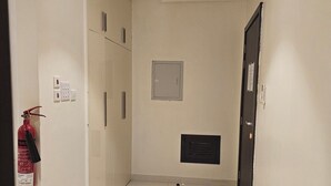 A narrow hallway with white tiled floors, a fire extinguisher on the left, a vent on the right, and a door at the end.