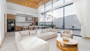 Un salon moderne avec un canapé d’angle, une table basse ronde et une vue sur la cuisine et l’espace extérieur.