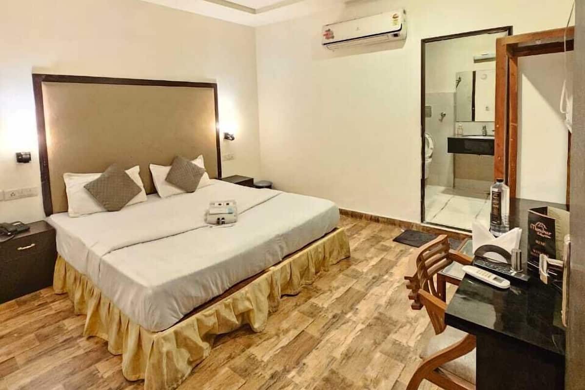 Habitación de hotel con cama, mesita de noche, escritorio, silla, ventilador de techo, aire acondicionado y espejo.