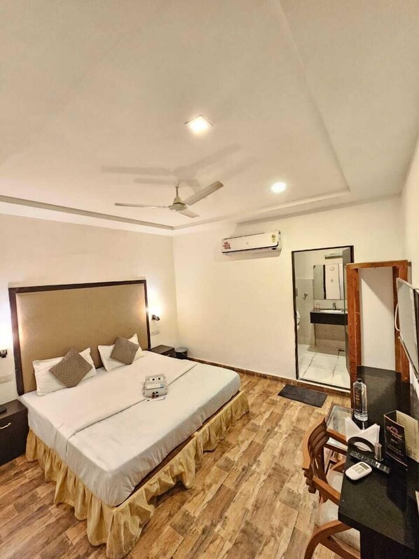 Una habitación de hotel con cama, escritorio, silla, ventilador de techo y aire acondicionado.