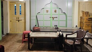 A room with a traditional thatched roof, a bed with a green headboard, a small stool, and a chair. - Manuhar (Jaipur)