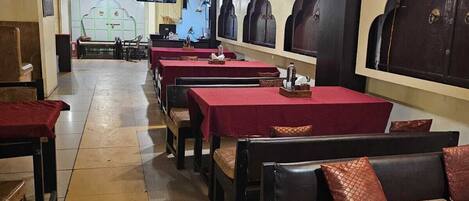 Un restaurante con varias mesas y cabinas, suelo de baldosas y una pantalla de televisión al fondo.