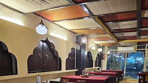 A restaurant with multiple tables and benches, a tiled floor, and a view of the outside through a glass door. - Manuhar (Jaipur)
