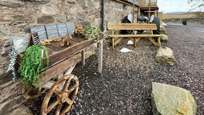 Ein rustikales Steinhaus mit einer Holzbank, einem Wagen mit Kreidetafeln und einer Schweineskulptur.