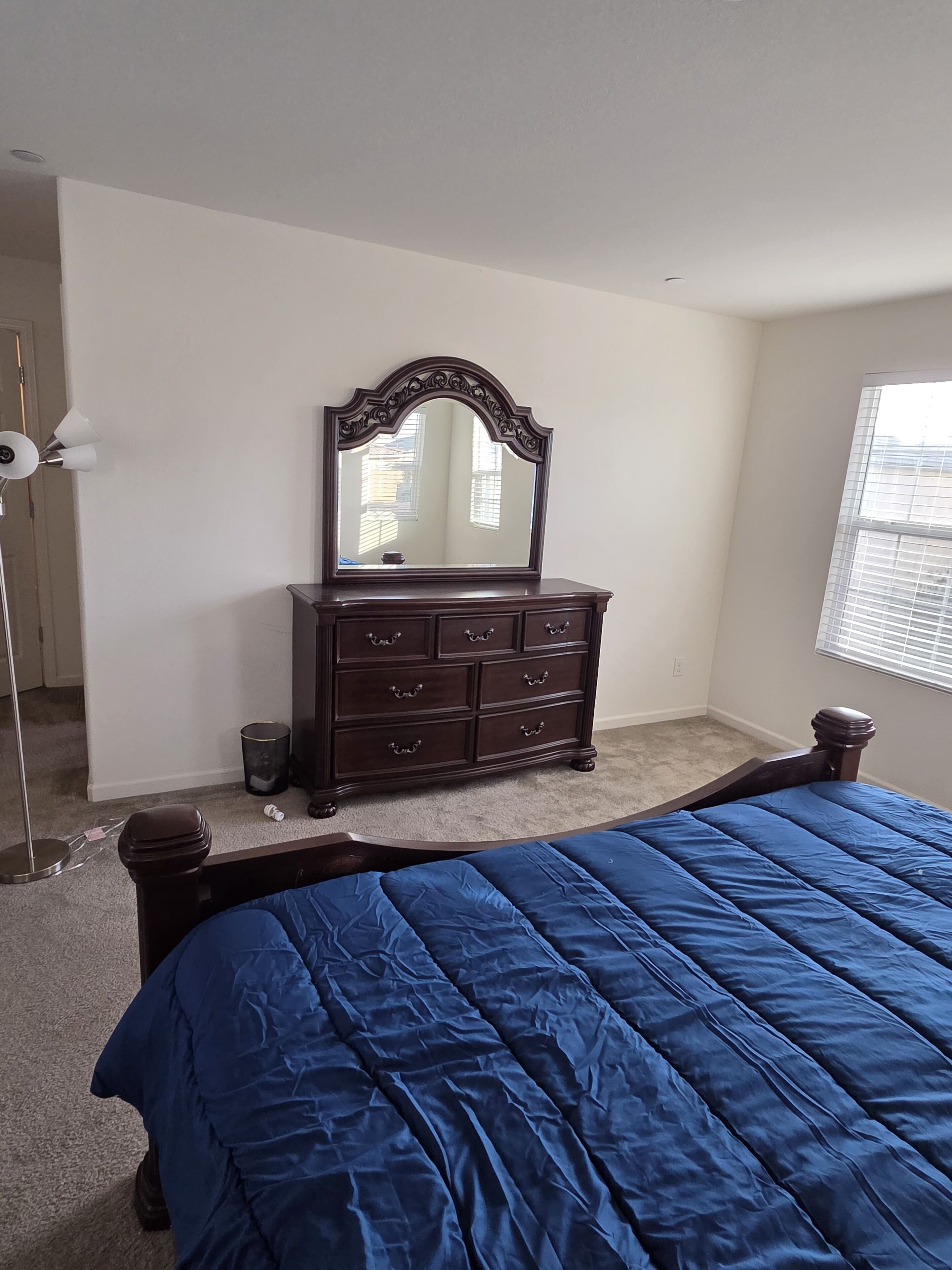 A bedroom with a bed, dresser, mirror, and window.