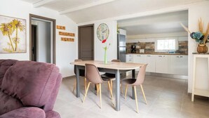 Een moderne woonkamer met een paarse bank, een houten eettafel met vier stoelen, en een keuken op de achtergrond.