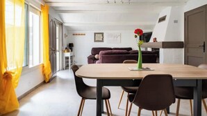 Een eethoek met een houten tafel en stoelen, een paarse bank achterin en een vaas met een rode bloem op de tafel.