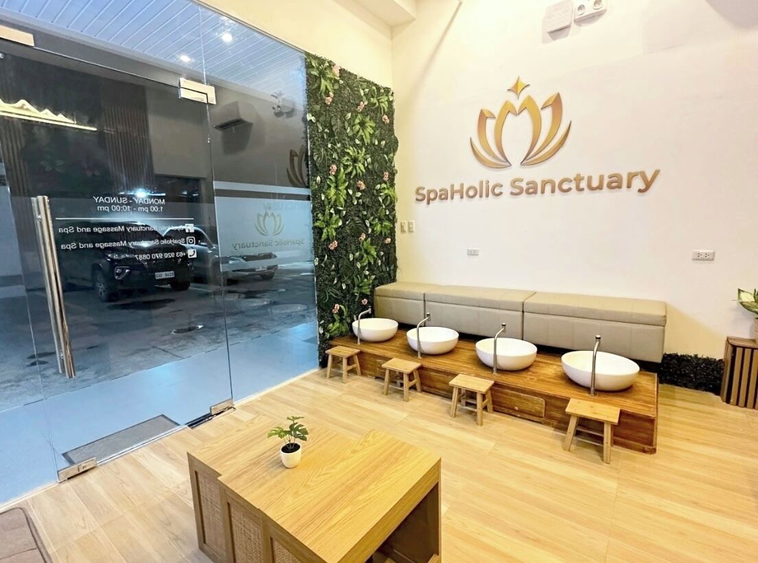 Zona de recepción de un spa, con mostrador, área de descanso y logotipo de SpaHolic Sanctuary en la pared.