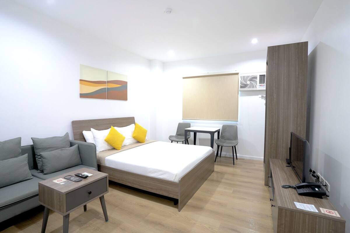 Quarto de hotel moderno com cama, escrivaninha, sofá e televisão.
